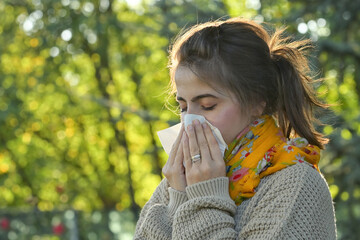 Girl in autumn park sneezing in tissue