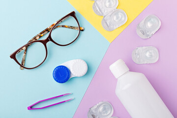 Contact lens kit with bottle of lens solution, case, tweezer on multicolor background, flat lay, top view