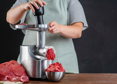 The cook puts the   meat in a meat grinder, minced  appears from the meat grinder. The process of cooking minced meat at home