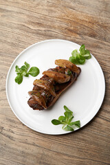 Toast with baked chicken liver on white plate on table