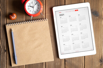 a tablet with an open calendar for 2021 year, a red alarm clock, chestnuts and a craft paper...