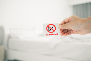 human's hand holding no smoking sign with blurred bedroom , in soft focus