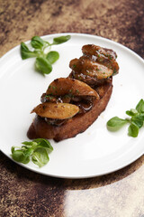 Toast with baked chicken liver on white plate on table
