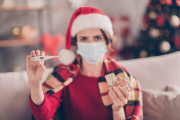 Fototapeta na wymiar Photo of cute young ill girl hold many packs meds thermometer wear mask santa cap red pullover decorated living room indoors