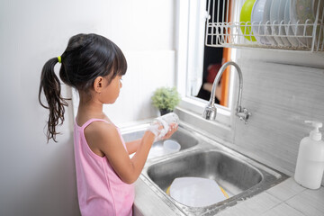 kid washing the dishes. helpful young girl doing clean up at home