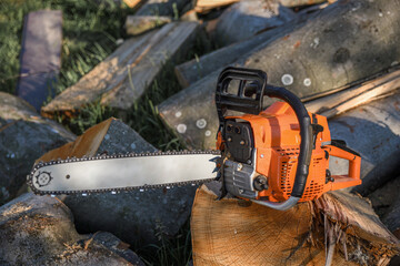 Naklejka premium Chainsaw that stands on a heap of firewood in the yard on a background of firewood and trees cut by a chainsaw