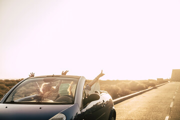 Freedom and happiness in a travel people lifestyle concept with couple of friends driving on a convertible car on a ong road with sunset in background - summer vacation together in friendship