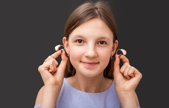 Teenage Girl Showing Her Modern Hearing Aids, Close-up On A Black Background. Selection Of Hearing Aids For A Child