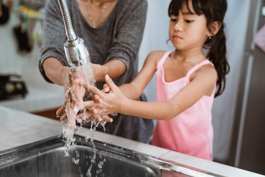 Mother And Daughter Wash Their Hand Together In The Kitchen Sink