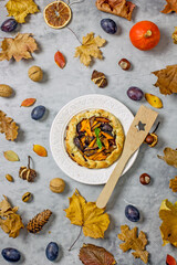 Autumn pie with plums and pumpkin on a light plate surrounded by fallen leaves, acorns, plums, linen napkins. Autumn still life with homemade cakes. Thanksgiving pie Top view, flat lay