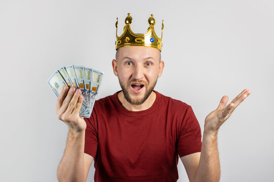 Young man in a golden crown holds money in his hands celebrates victory on a light background. Concept  king, luck, gain, rich, dream, goal, aspiration, bet. Banner