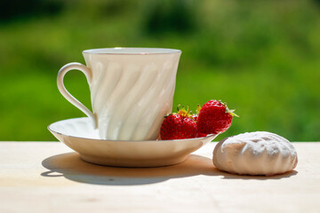 Elegant white porcelain Cup with a Saucer and Strawberries on a wooden Terrace against the background of Nature. Russian Imperial Porcelain.