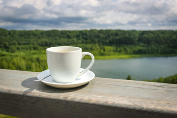 White cup of hot coffee on balcony with natural and mountains, hills background. Copy space.