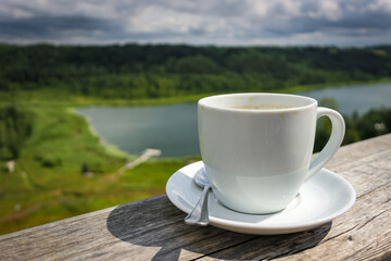 White cup of hot coffee on balcony with natural and mountains, hills background. Copy space.
