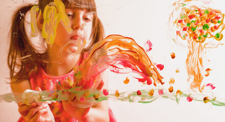 Beautiful young girl painting artwork on glass with colorful finger. Happy childhood, art, painting lessons concept.