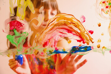 Obraz premium Beautiful young girl painting artwork on glass with colorful fingers. Happy childhood, art, painting lessons concept. Selective focus on finger.