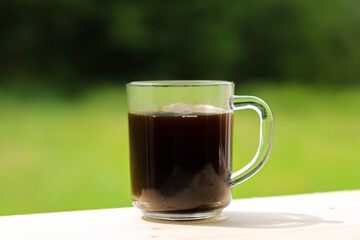 A glass transparent cup with black coffee, from which steam is rising.