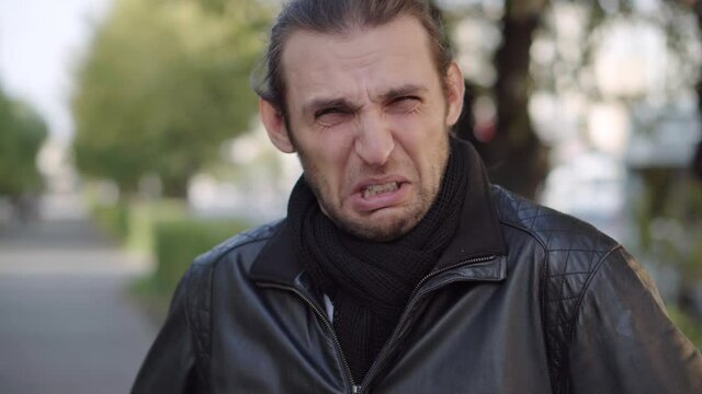 Young man in black jacket expressing disgust and disapproval with negative facial expressions outdoors.
