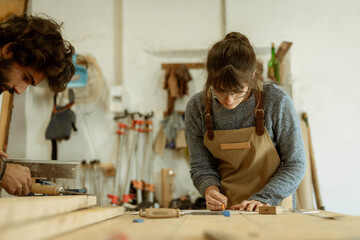 A young couple of carpenters working together in a small carpentry workshop designing a new home furniture piece crafting out of timber. Young entrepreneurs running their own business in Lisbon