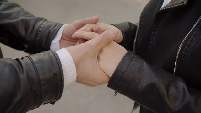 Close-up of the hands of a young love couple when they meet on the street. Romantic moment between two lovers.