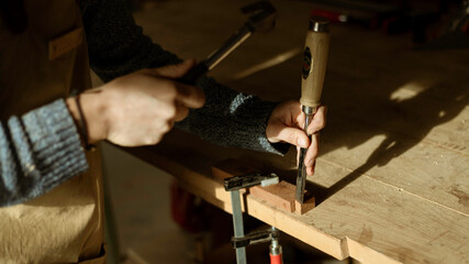 Close up of carpenter hands working with a hammer in a small carpentry workshop. Young wood worker woman working on a piece of timber for a new home design project. Entrepreneurs concept