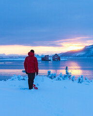 A man with snowshoes under moody sky winter sunset blue hour over the red houses in Norway