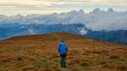 Tourist with large blue backpack walking on a mountain ridge towards a horizon, Low Tatras, Slovakia.