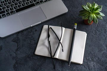 on the table is an open notebook, a pencil and glasses. There is a laptop nearby