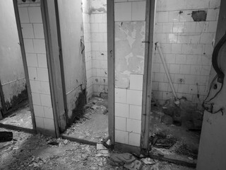 Interior of an old messy abandoned and ruined toilet with cabins, broken doors and missing sanitary ware