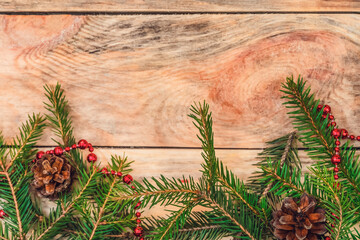 Christmas tree branches on a wooden background with cones, red beads on the bottom with copy space, top view