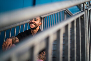 Chico joven tatuado en escaleras metálicas junto a edificio azul