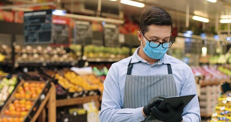 Portrait of Caucasian handsome male food store manager in medical mask and gloves standing in...