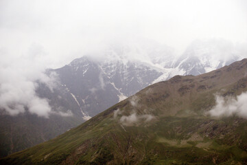 Fototapeta premium Peaks and slopes of mountains in foggy weather. Elbrus region near the village of Terskol. Caucasus, Russia.