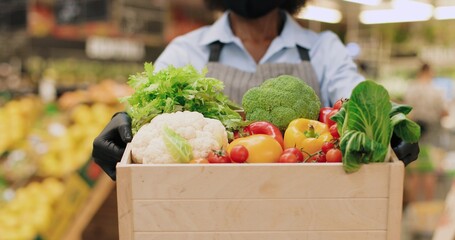 Close up of African American woman hands holding box with vegetables while standing in food store. Female in face mask holding different food in supermarket indoors. Retail concept
