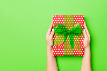 Top view of female hands holding christmas or other holiday handmade present box package in the palms, flat lay table background with copy space