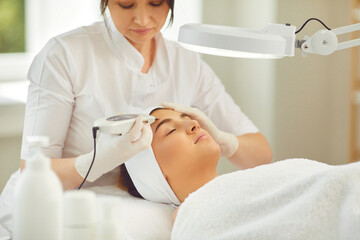 Woman dermatologist doing ultrasound apparatus facial cleaning with special machine for young woman