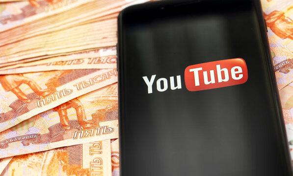 YouTube logo on the sceen smartphone and russian money, rubles closeup. YouTube is a free video sharing application that anyone can watch. Moscow, Russia - August 11, 2020