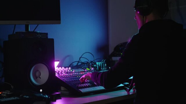 A professional DJ or producer with headphones creates music in the studio behind a mixing console. Dancing, waving his arms. The artist makes creativity. Recorded a new track