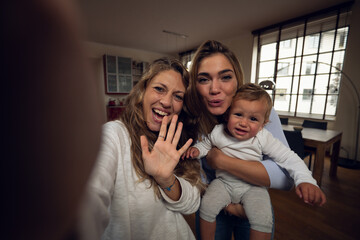 A happy smiling family is making a selfie or video call to friends or relatives while having a breakfast together in a living room at home.