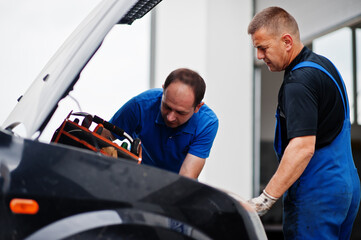 Fototapeta na wymiar Car repair and maintenance theme. Two mechanics in uniform working in auto service, checking engine.
