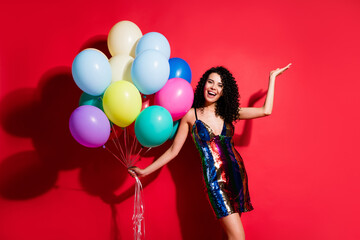 Obraz na płótnie Canvas Full length photo of gorgeous girl hold many balloons raise arm palm wear glossy short dress isolated bright red color background