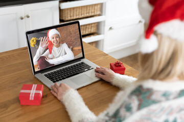 Woman in Santa hat having a video chat with another woman on her laptop at home