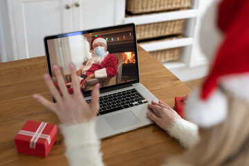 Woman in Santa hat having a video chat with Santa Claus wearing face mask on her laptop at home