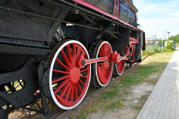 Naklejka premium Close up on a set of red and white wheels of an old black and red train standing on a side track seen on a sunny summer day in Poland next to an abandoned train station 