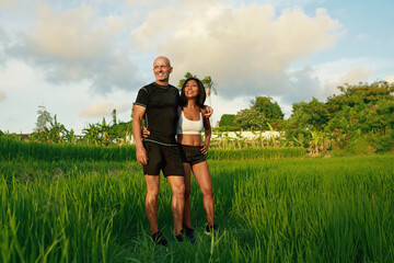 Mature Couple’s Standing On Rice Field Portrait. Caucasian Man And Asian Woman Resting After Workout In Morning Against Tropical Landscape.