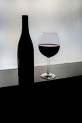 Wine glass and a bottle on a black table  in front of the window, isolated