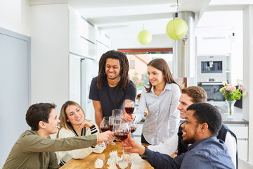 Happy friends toasting together with glass of red wine in kitchen