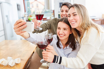Happy girlfriends with red wine make selfie together in kitchen