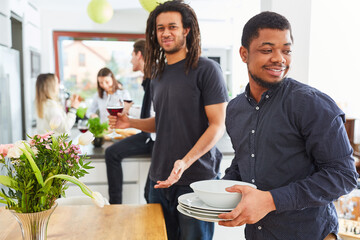 African man with dishes at table setting in kitchen with friends