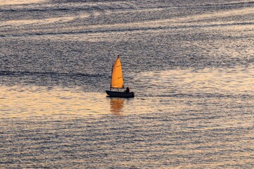 Lonely sailing yacht on the river in the light of the sunset. Beautiful evening landscape.